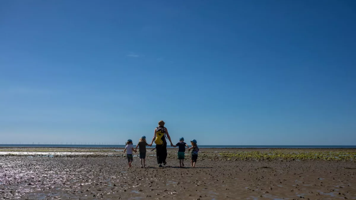 children and a teacher walking across the beach holding hands