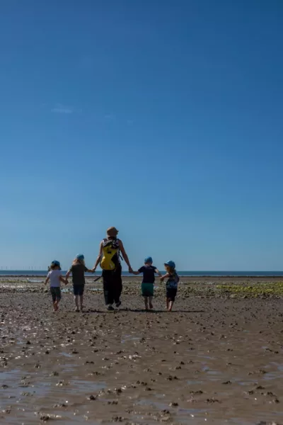 children and a teacher walking across the beach holding hands