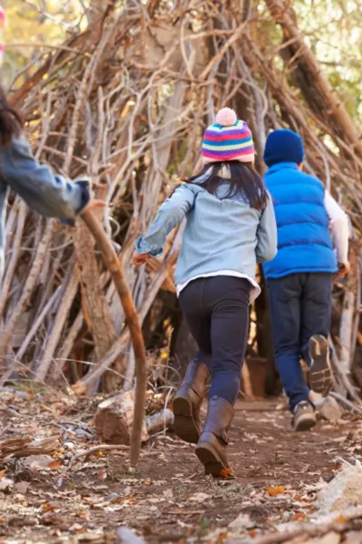 Children running into den made with branches