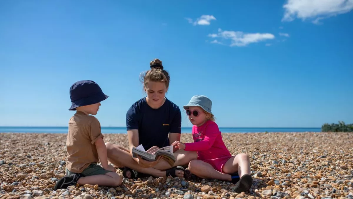 2 children reading a book with a teacher